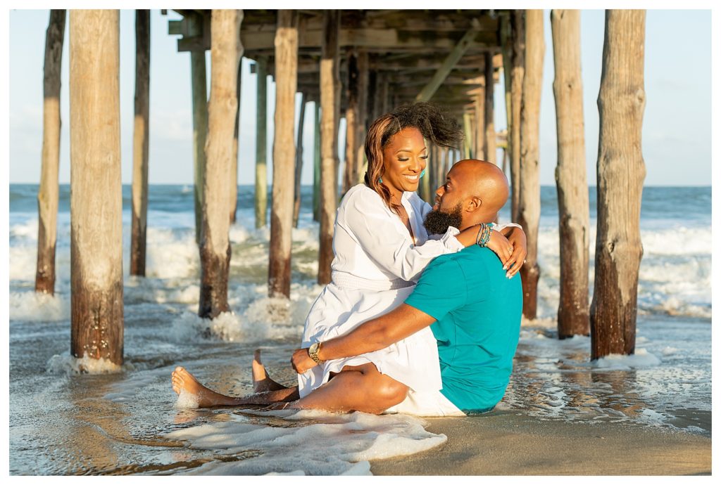 African American couple posed sitting in the water during their engagement session smiling.